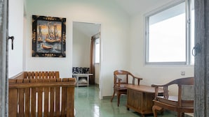 Une pièce comprenant un banc en bois, deux chaises en bois, une table et un tableau représentant un navire accroché au mur.