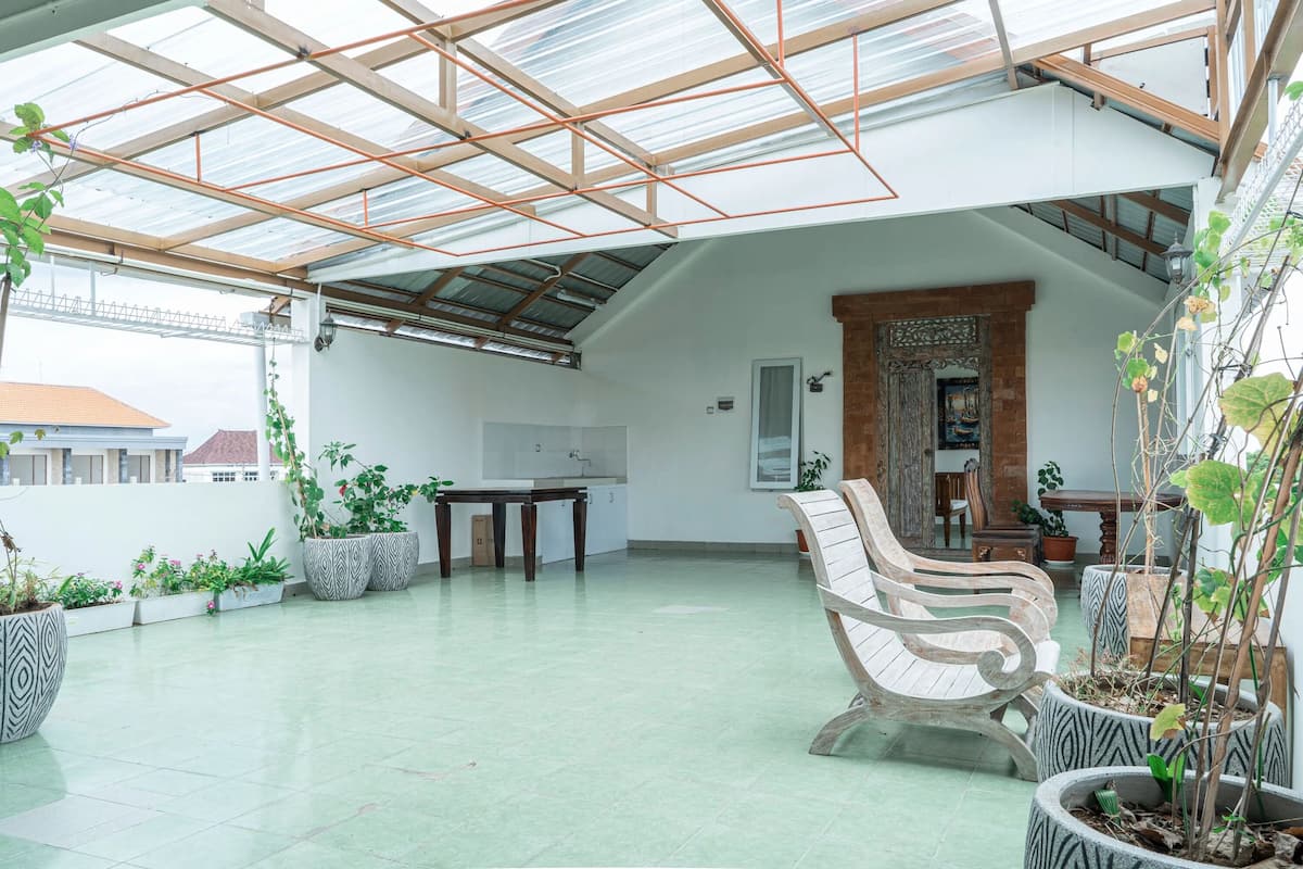 A spacious covered patio with a high ceiling, potted plants, a wooden bench, and a dining table.