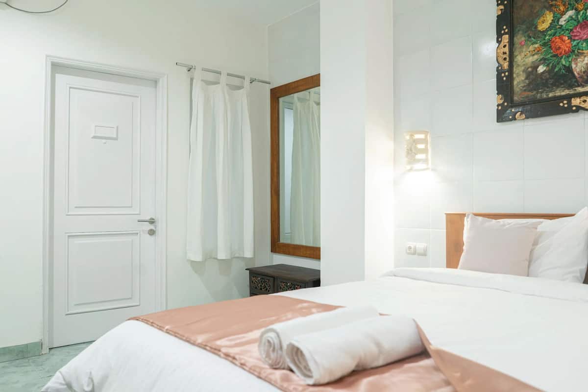 A hotel room with a bed, a door, a small table, and a painting on the wall.