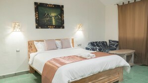 Un lit bien fait, avec une tête de lit en bois, un tableau accroché au-dessus et deux lampes fixées au mur.