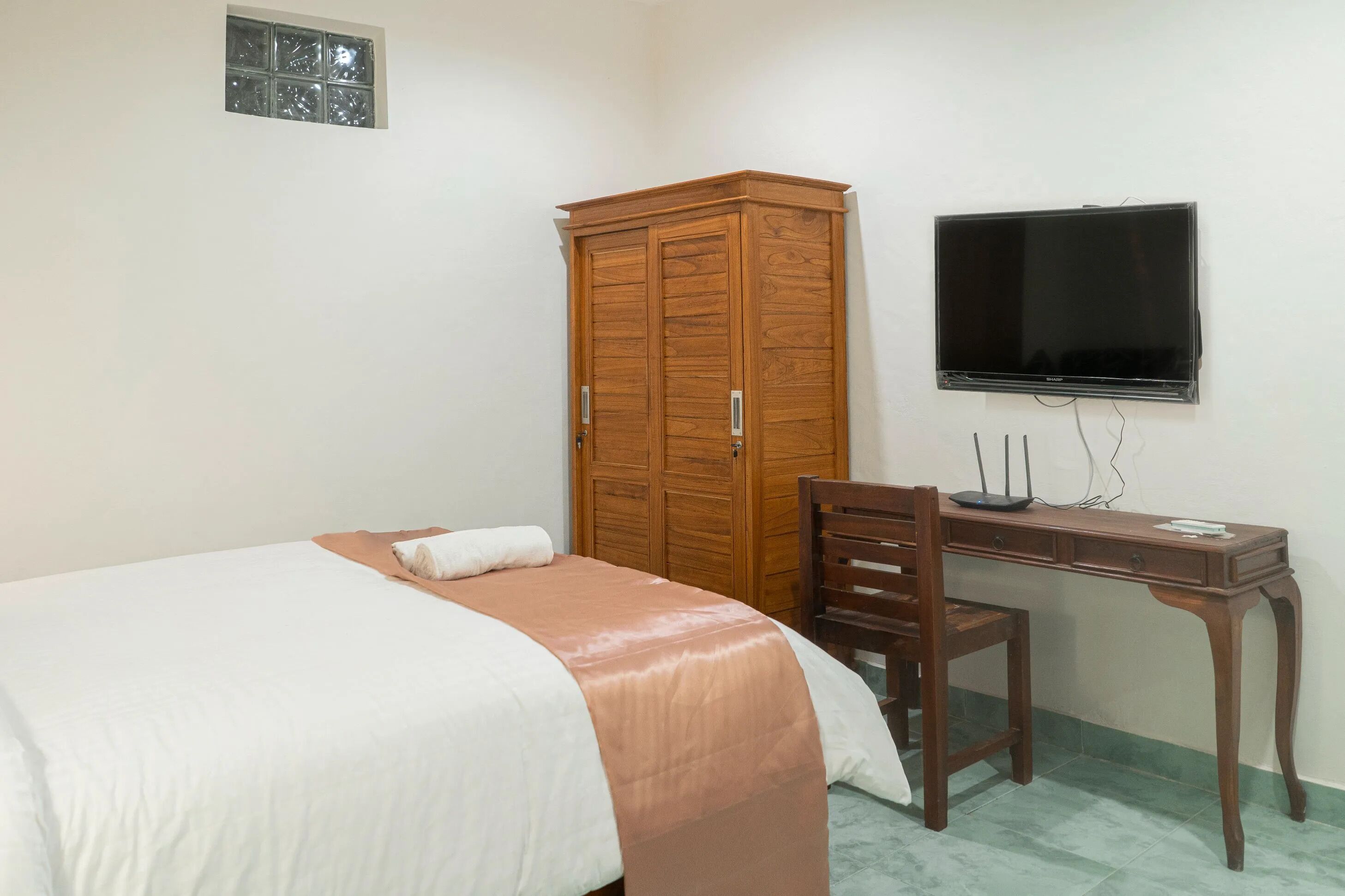 Ein Schlafzimmer mit einem Bett, einem Holzschrank, einem Schreibtisch mit Stuhl und einem an der Wand befestigten Fernseher.
