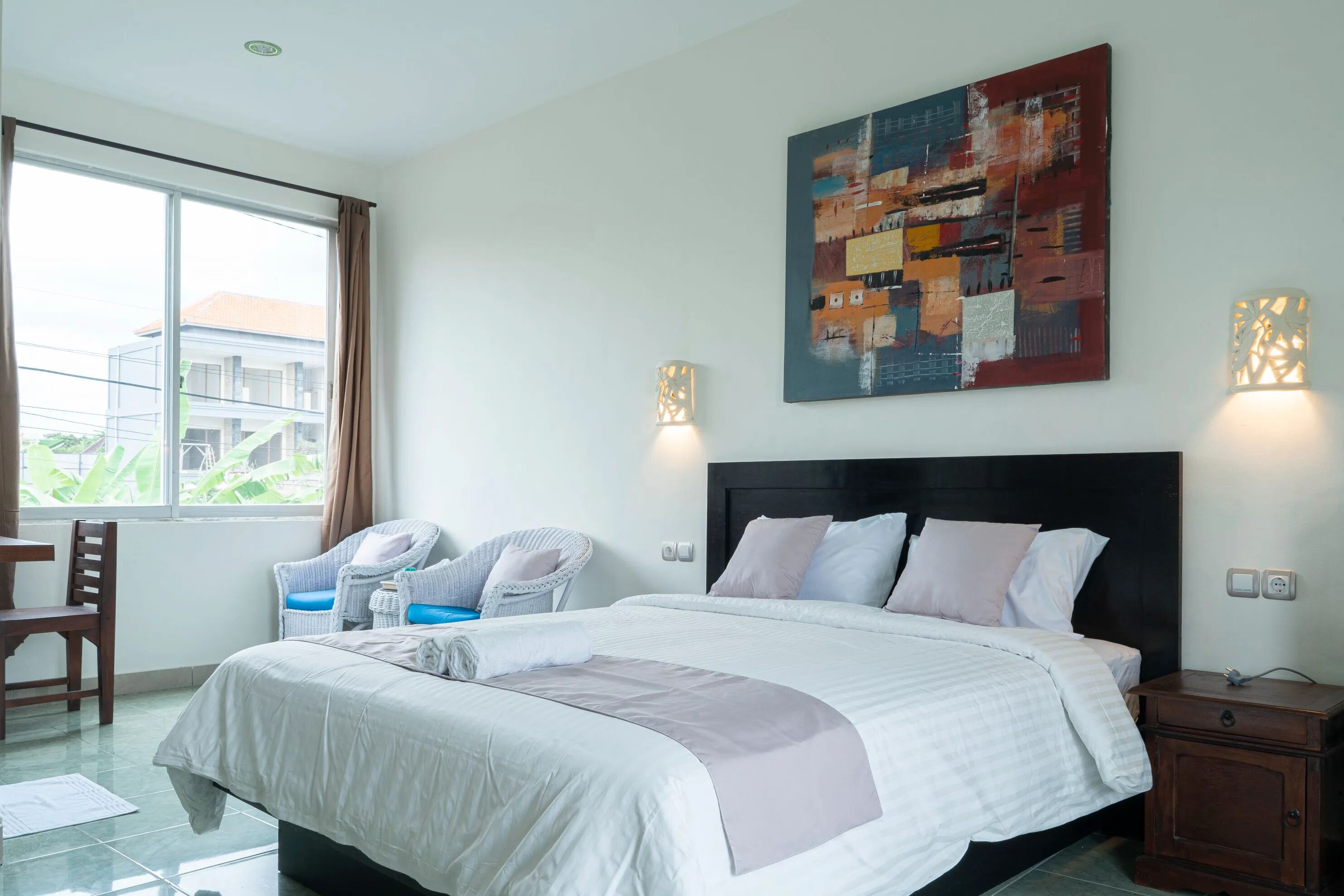 A modern hotel room with a large bed, a desk, a chair, and a view of the outside.