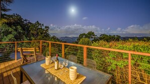 A table set for two with a bottle and glasses, overlooking a scenic view of a city and the ocean under a night sky. - The Hillside Retreat, with amazing coastal and hinterland view. (Tamborine Mountain)