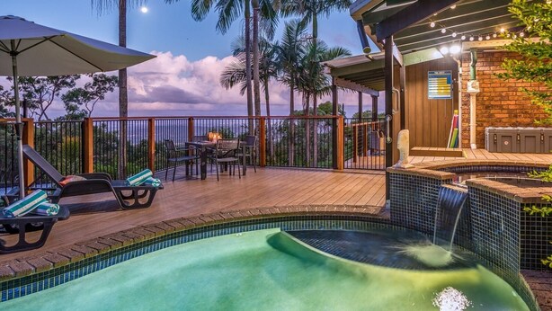 A swimming pool with a waterfall feature, surrounded by lounge chairs and a deck area with a table and chairs. - The Hillside Retreat, with amazing coastal and hinterland view. (Tamborine Mountain)