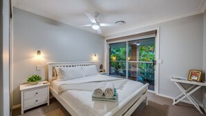 A bedroom with a large bed, a ceiling fan, a nightstand with a lamp, and a view of a garden through a sliding door. - The Hillside Retreat, with amazing coastal and hinterland view. (Tamborine Mountain)