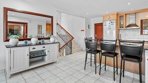 A modern kitchen with white cabinetry, a wooden staircase, and a dining area with black chairs. - San Lameer Villa 10902 Private Pool  (Southbroom)