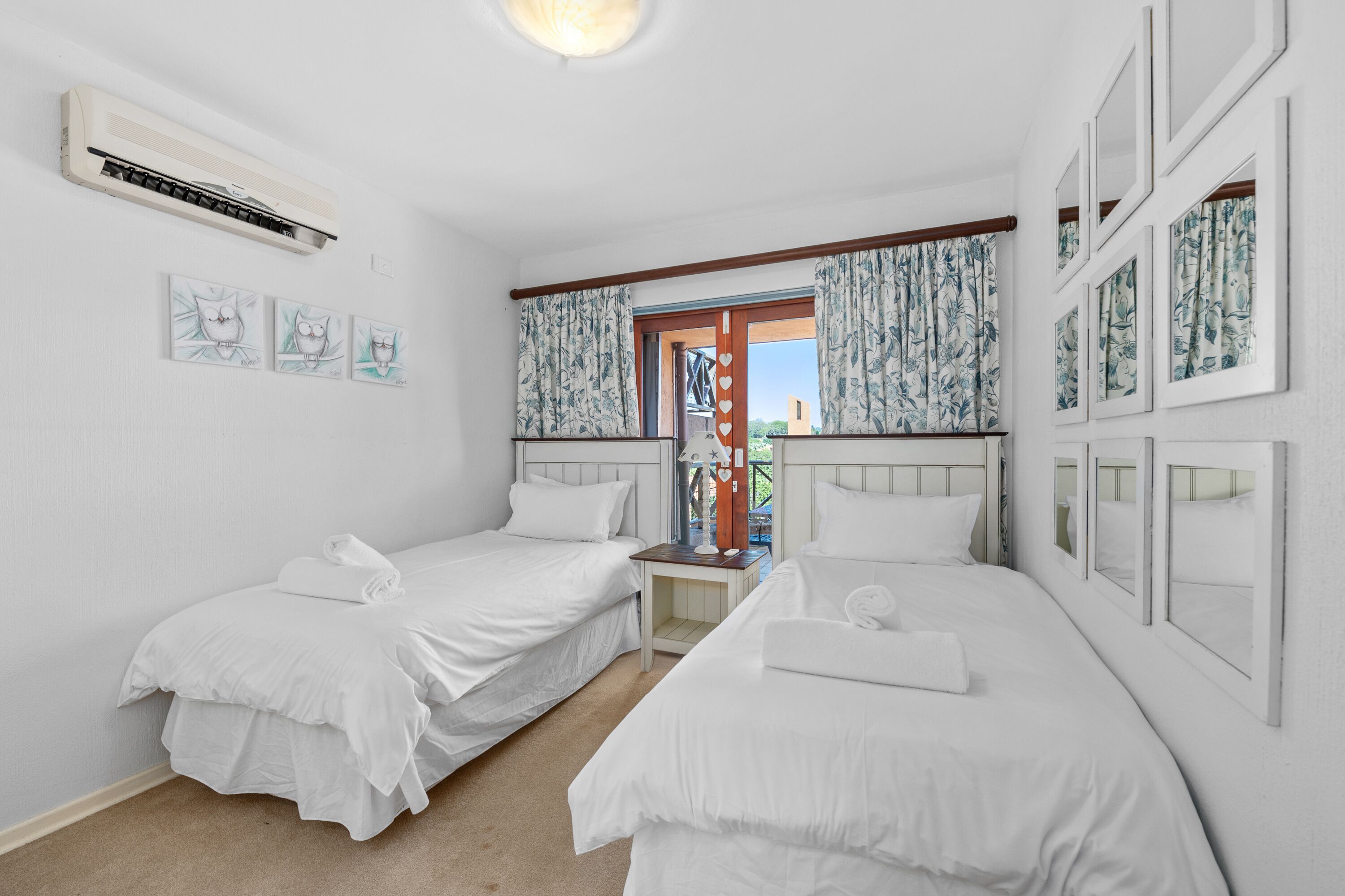 Een hotelkamer met twee eenpersoonsbedden, een kleine tafel, een wandairconditioner en een raam met gordijnen.
