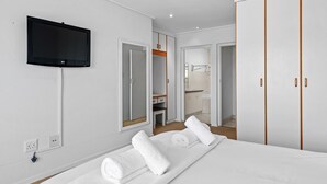 A modern hotel room with a bed, a flat-screen TV mounted on the wall, a walk-in closet, and a bathroom visible through an open door. - San Lameer Villa 10902 Private Pool  (Southbroom)