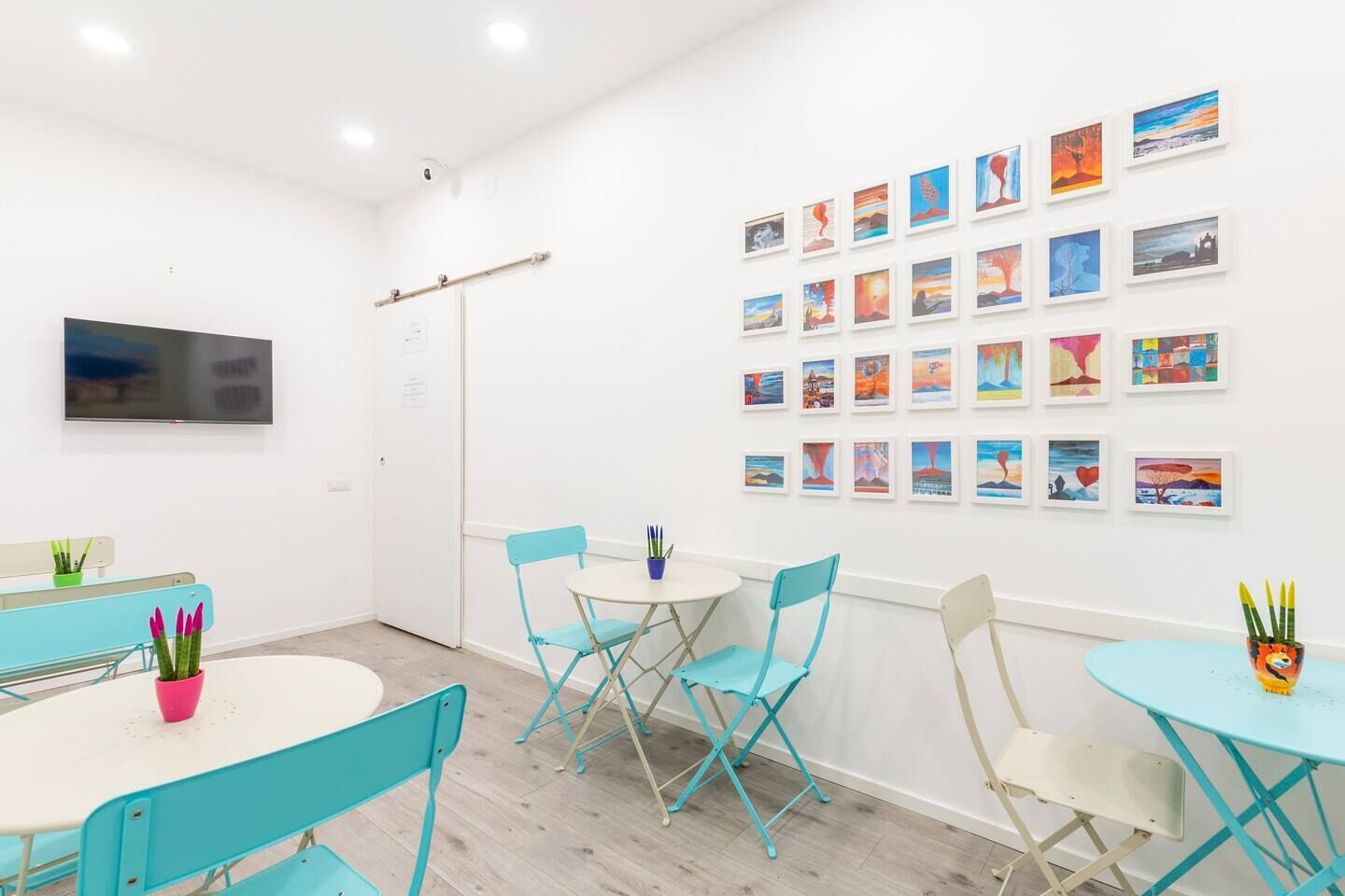 Een moderne kamer met teal stoelen, een witte tafel en een wand versierd met ingelijste kunstwerken.