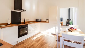 A modern kitchen with white cabinetry, a built-in oven, a microwave, and a black range hood. - The Milking Parlour (Cranbrook)