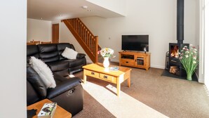 A living room with a black leather sofa, a wooden coffee table, a TV, a fireplace, and a staircase. - The Milking Parlour (Cranbrook)
