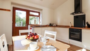 A modern kitchen with a dining area, wooden flooring, and a large window providing natural light. - The Milking Parlour (Cranbrook)