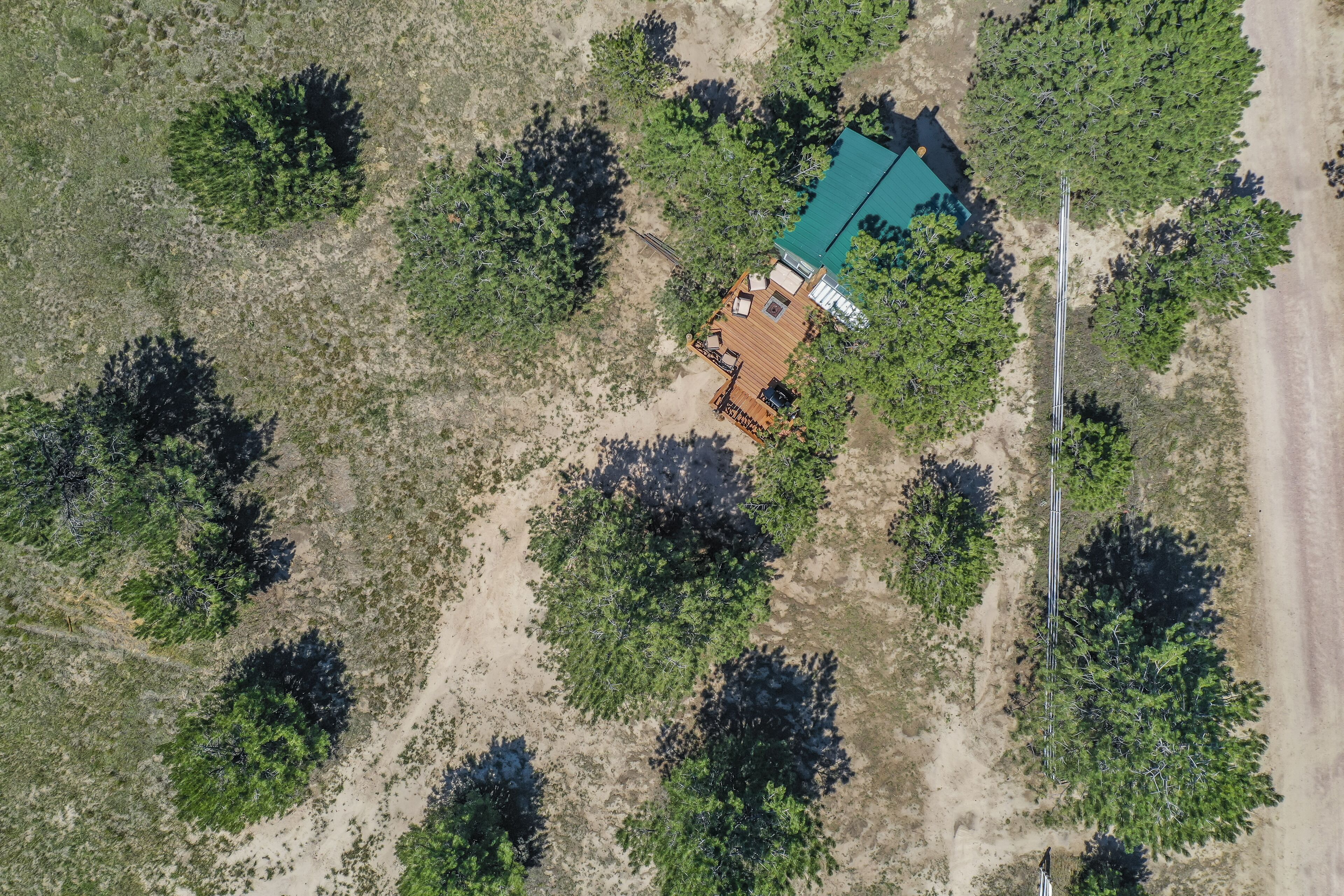 Vista aérea de una cabaña con terraza y zona de estar al aire libre rodeada de árboles.