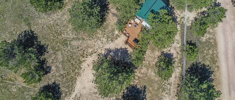 An aerial view of a cabin with a deck and outdoor seating area surrounded by trees.