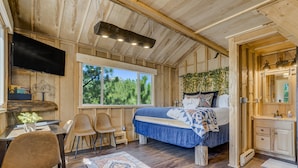 A wooden cabin interior with a bed, desk, chairs, and a TV. - Tree Eagles Nest (Larkspur)