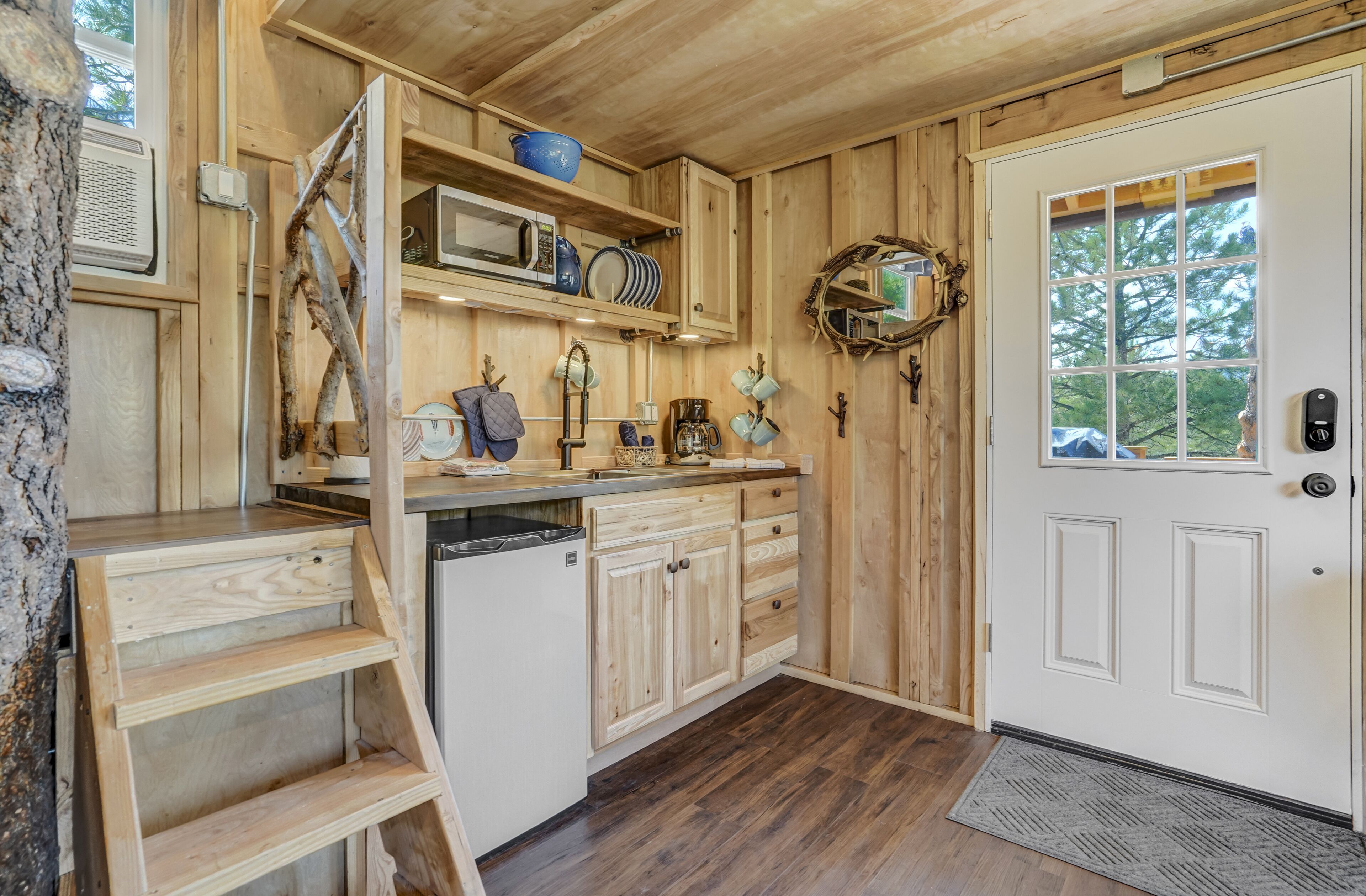 Un interior de madera con una zona de cocina, que incluye un microondas, estantes y una puerta con ventanal.