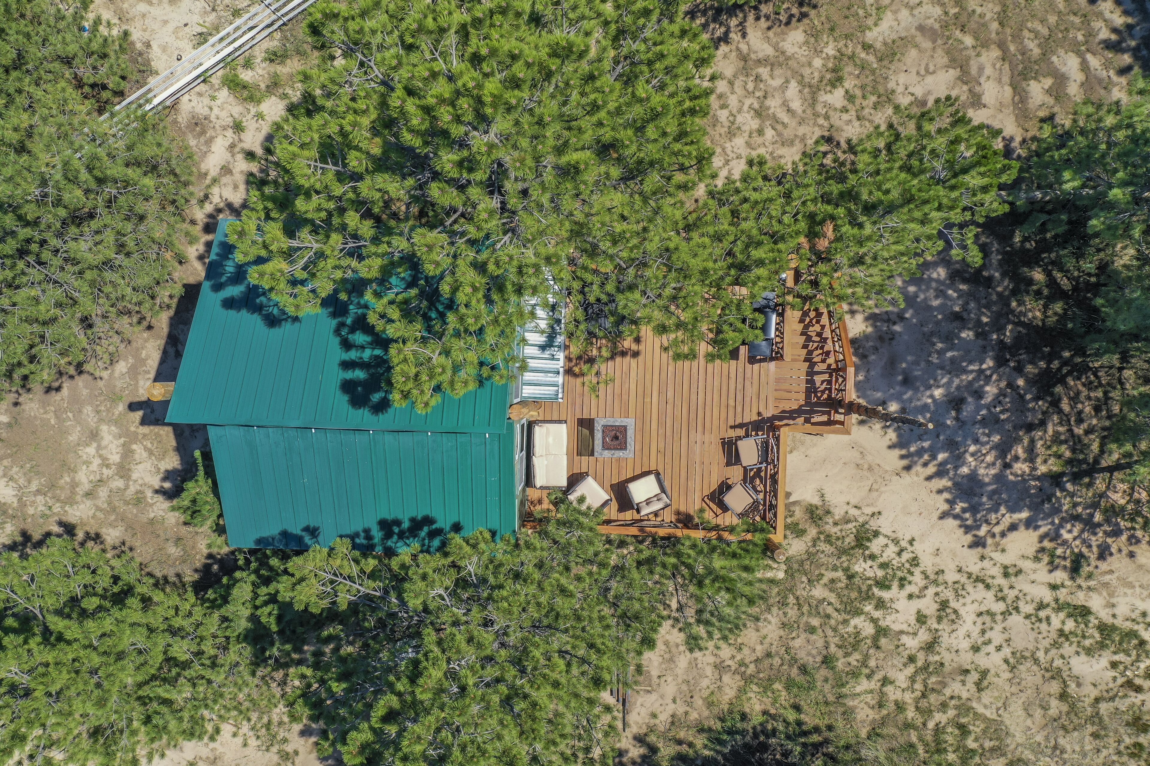 An aerial view of a cabin with a green roof, surrounded by dense forest.