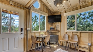 A cozy cabin interior with a fireplace, wooden walls, and large windows offering views of pine trees. - Tree Eagles Nest (Larkspur)