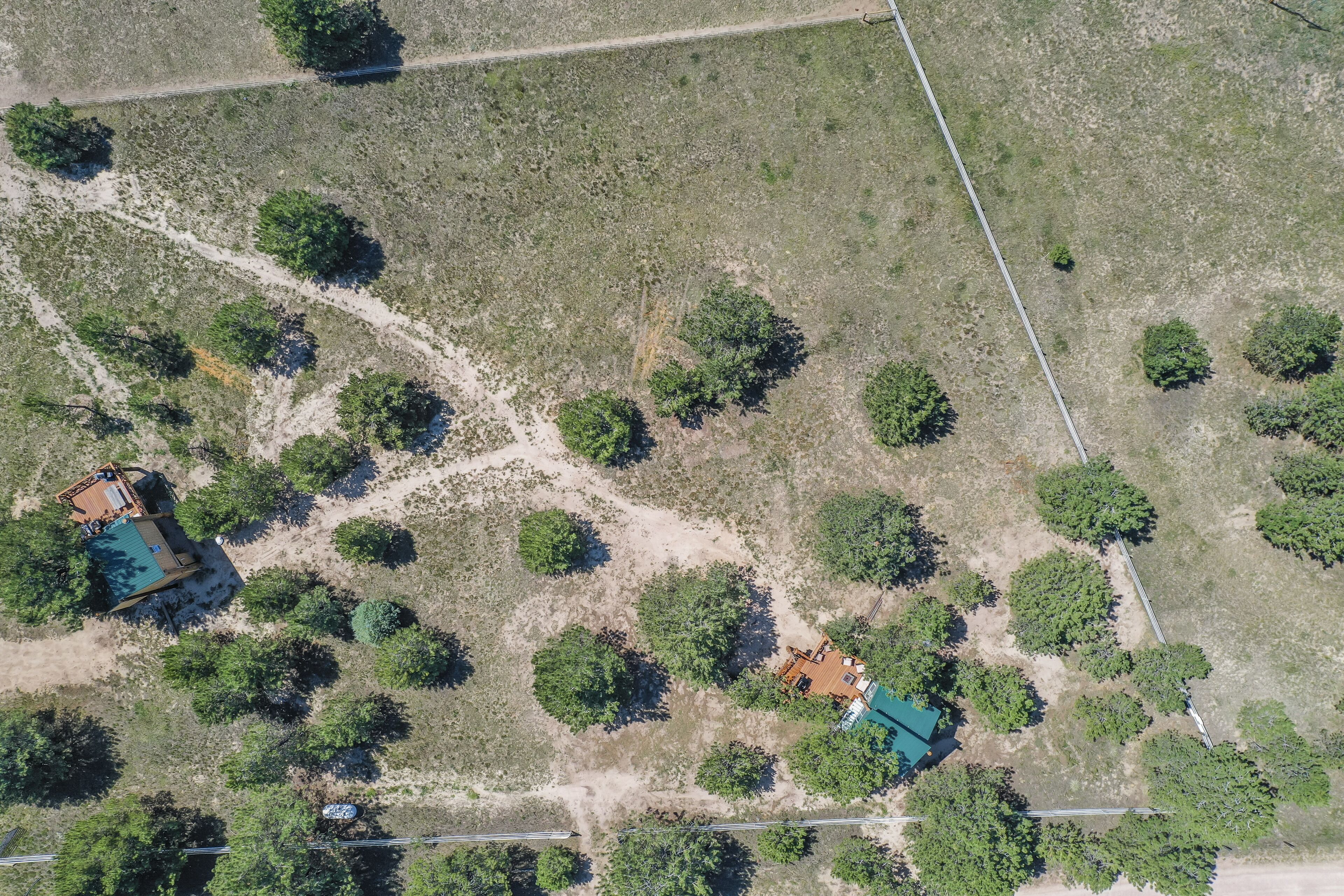 An aerial view of a property with two main buildings, a swimming pool, and scattered trees.