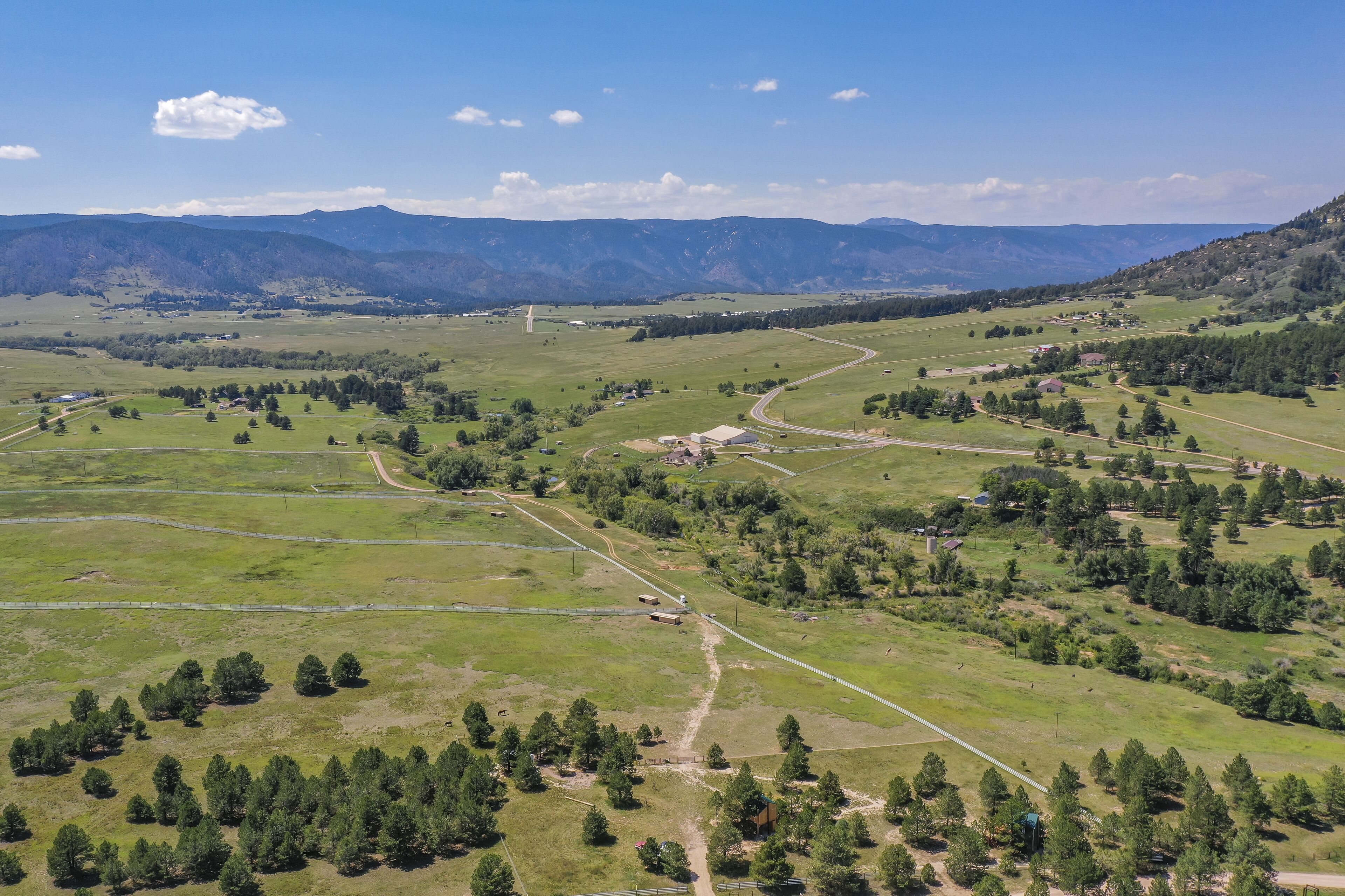 Un paysage rural caractérisé par des collines douces, une route sinueuse et des bâtiments dispersés.