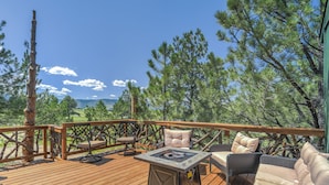 A wooden deck with outdoor furniture, including a table and chairs, overlooking a mountainous landscape. - Tree Eagles Nest (Larkspur)