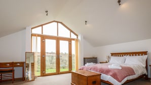 Ein Schlafzimmer mit schrägem Dach, einem großen Fenster, einem Bett, einem Schreibtisch und einer Kommode.