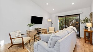 A modern living room with a grey sofa, a striped armchair, a wooden coffee table, and a TV mounted on the wall. - Newly furnished Condo in Heart of Palm Desert! Pool, PickleBall! (Palm Desert)