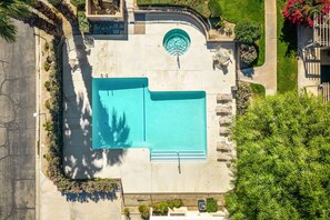 Blick von oben auf einen Poolbereich mit einem runden Whirlpool, umgeben von einer Hecke und Grünpflanzen.