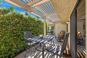 Eine Terrasse im Freien mit Tisch und Stühlen, umgeben von Grünpflanzen und einem Pergola-Überbau.