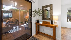 A modern interior with a glass door leading to a living area, a wooden console table with a mirror, and a potted plant. - Newly furnished Condo in Heart of Palm Desert! Pool, PickleBall! (Palm Desert)