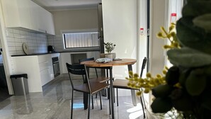A modern kitchen with white cabinets, a round wooden table, and two chairs. - Granny Guest House Sydney Blue Mountain (Kingswood)
