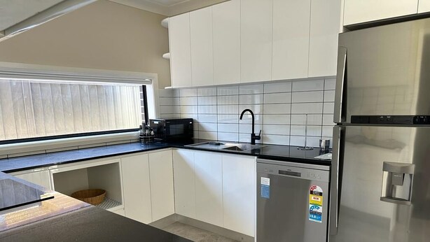 A modern kitchen with white cabinets, a stainless steel refrigerator, a dishwasher, and a microwave. - Granny Guest House Sydney Blue Mountain (Kingswood)