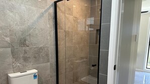 A bathroom with a glass-enclosed shower, a toilet, and a tiled floor. - Granny Guest House Sydney Blue Mountain (Kingswood)