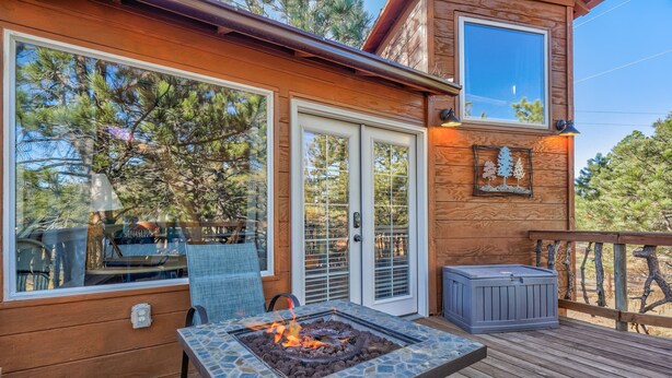 Une terrasse en bois avec un foyer, des sièges d’extérieur et une vue sur les arbres.