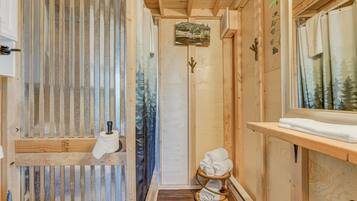 A wooden cabin bathroom with a shower, a towel rack, and a small shelf with towels.