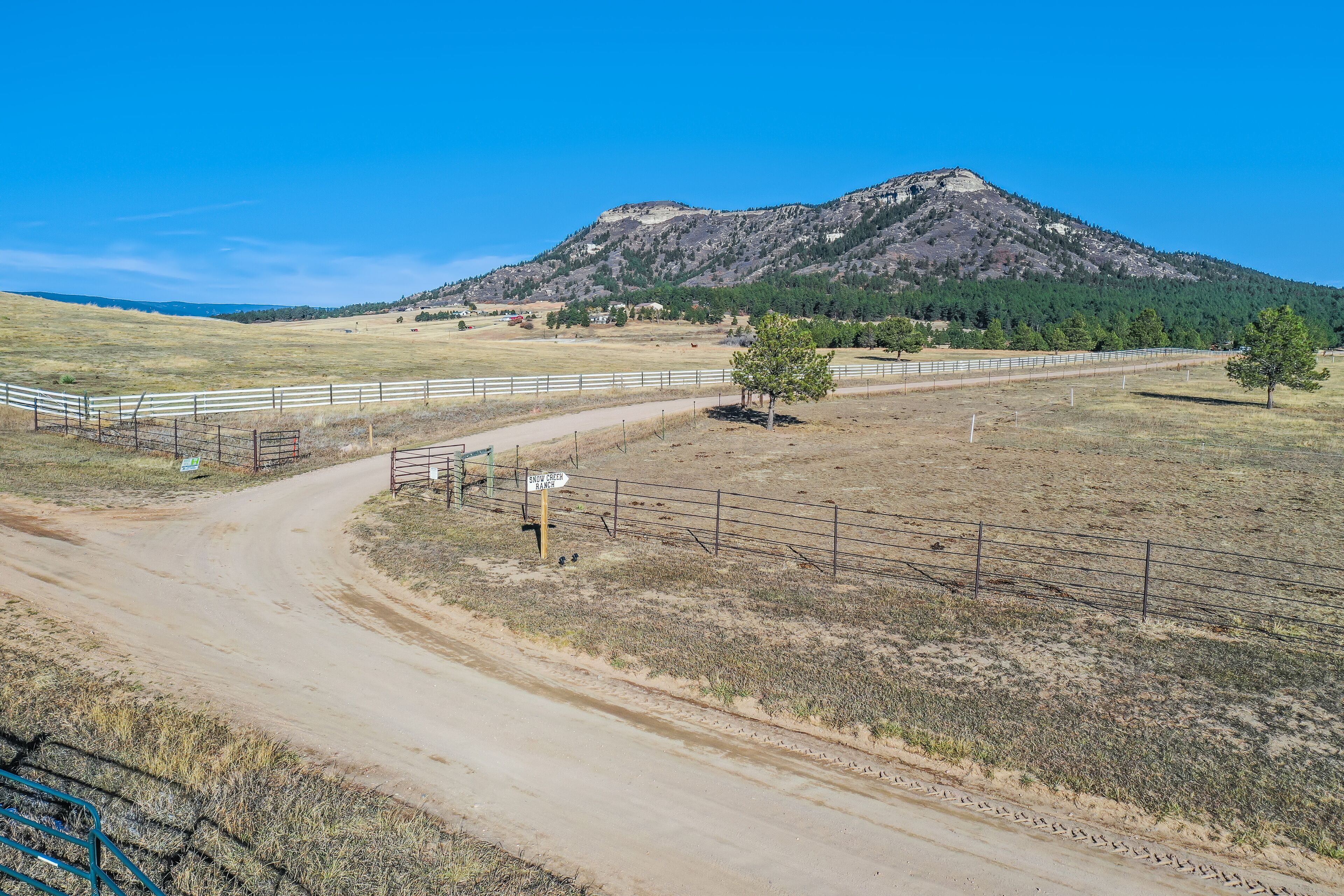 A dirt road leading to a fenced area with a mountain in the background.