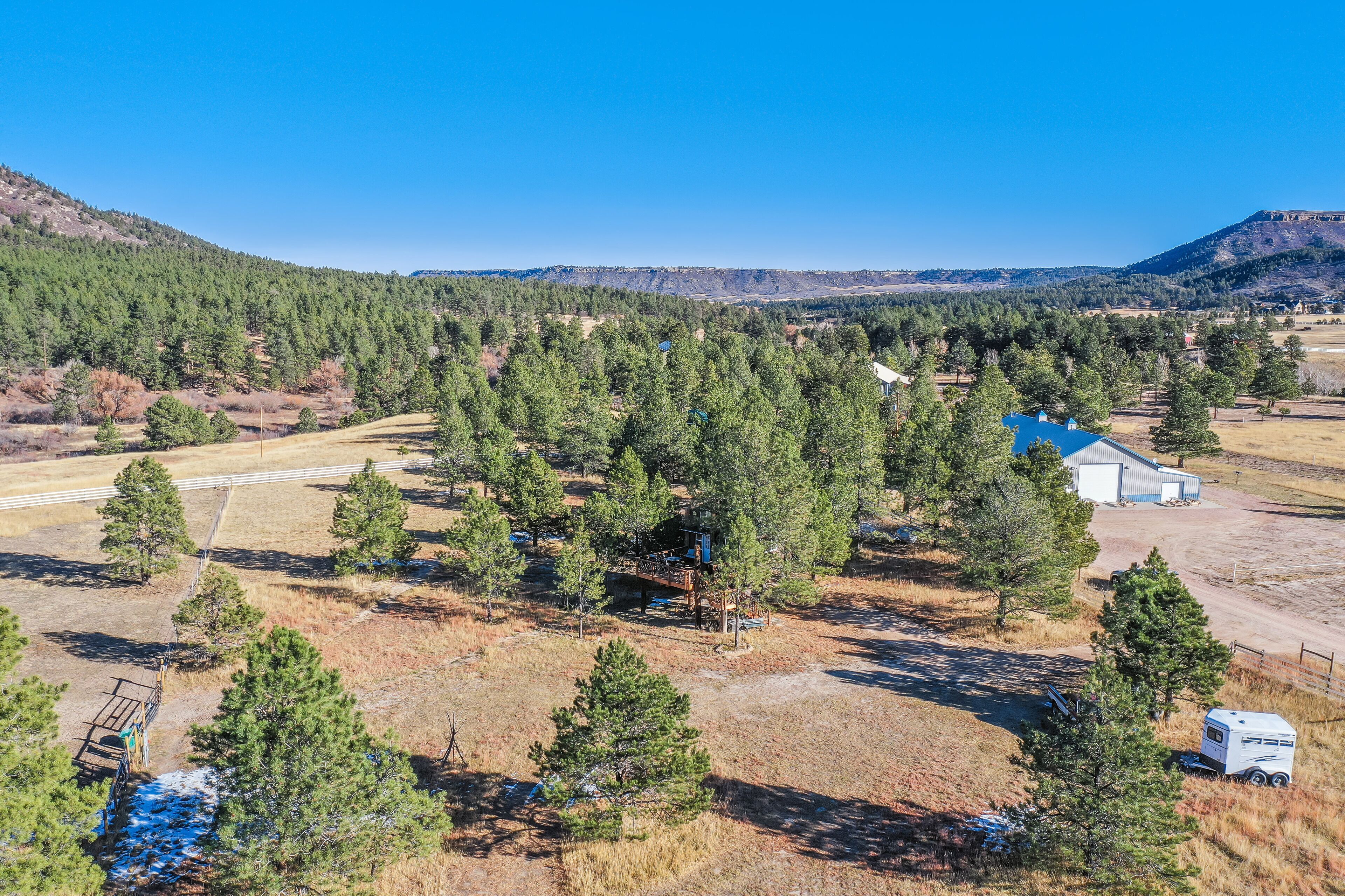 An aerial view of a rural property with a large barn, several trees, and a trailer.