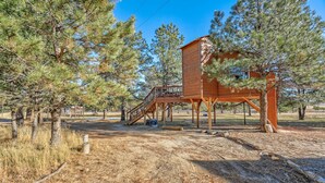 Une cabane en bois avec un escalier et une terrasse, entourée de pins.