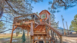 Une cabane en bois perchée dans un arbre, avec un escalier et un petit espace clos en haut.