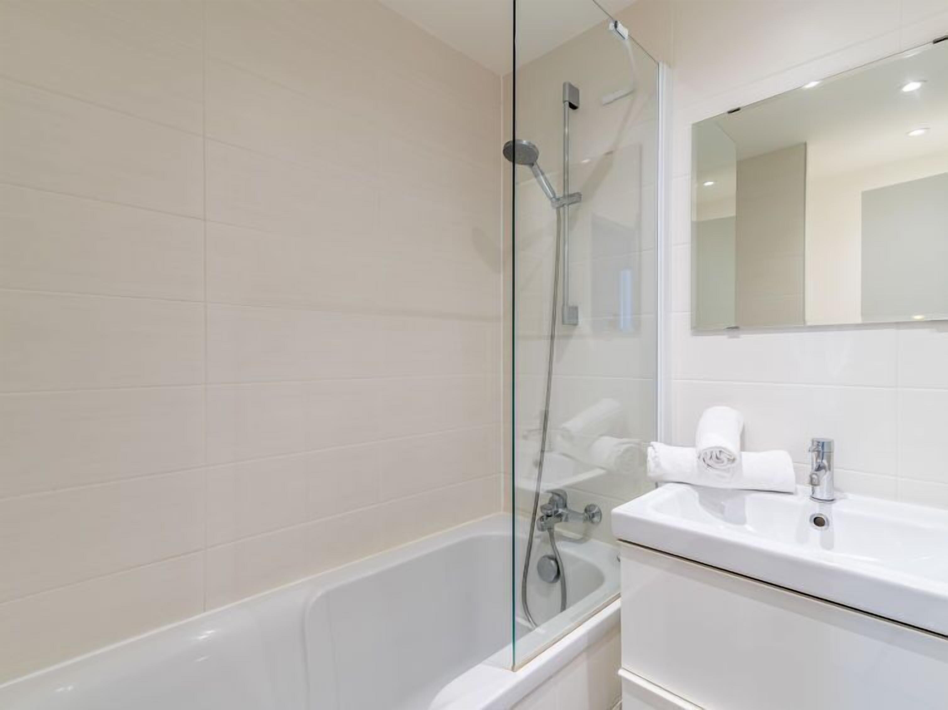 A modern bathroom with a glass-enclosed shower, a white bathtub, and a sink with a mirror above it.