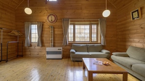 Interior acogedor de una cabaña con piso de madera, un sofá, una mesa, un calentador y una ventana con cortinas.
