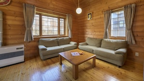 Interior de una cabaña de troncos con dos sofás, una mesa de centro de madera y un ventanal con cortinas.