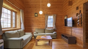 Una habitación acogedora de estilo cabaña, con paredes y suelos de madera, que incluye dos sofás, una mesa de centro, un televisor de pantalla plana y una chimenea.