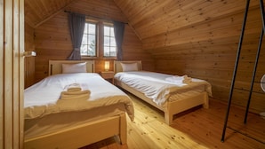 Una habitación de cabaña acogedora con dos camas de madera, una ventana con cortinas y un ventilador de pie.