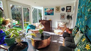 Ein geräumiges Wohnzimmer mit großem Fenster, Korbsesseln, einem runden Couchtisch und verschiedenen Topfpflanzen.