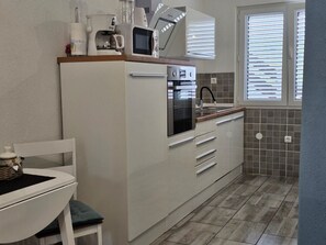 Compact kitchen with microwave, coffee maker, and stainless steel oven, sink, and window with blinds.