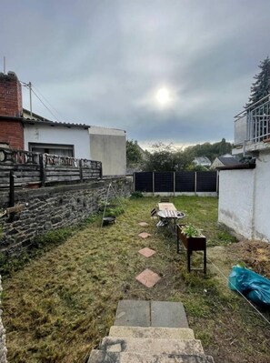 outdoor space with a table and chairs, surrounded by lush greenery and a stone wall.