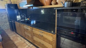 A kitchen with a black stove, a microwave, and wooden cabinets. - Casa Obis - Casa Rural con Jardín, Barbacoa y Unas Espectaculares Vistas (Muñeca)