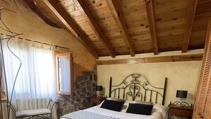 A cozy bedroom with a wooden ceiling, a stone wall, a bed with a white and gray striped bedspread, and a bench by the window. - Casa Obis - Casa Rural con Jardín, Barbacoa y Unas Espectaculares Vistas (Muñeca)