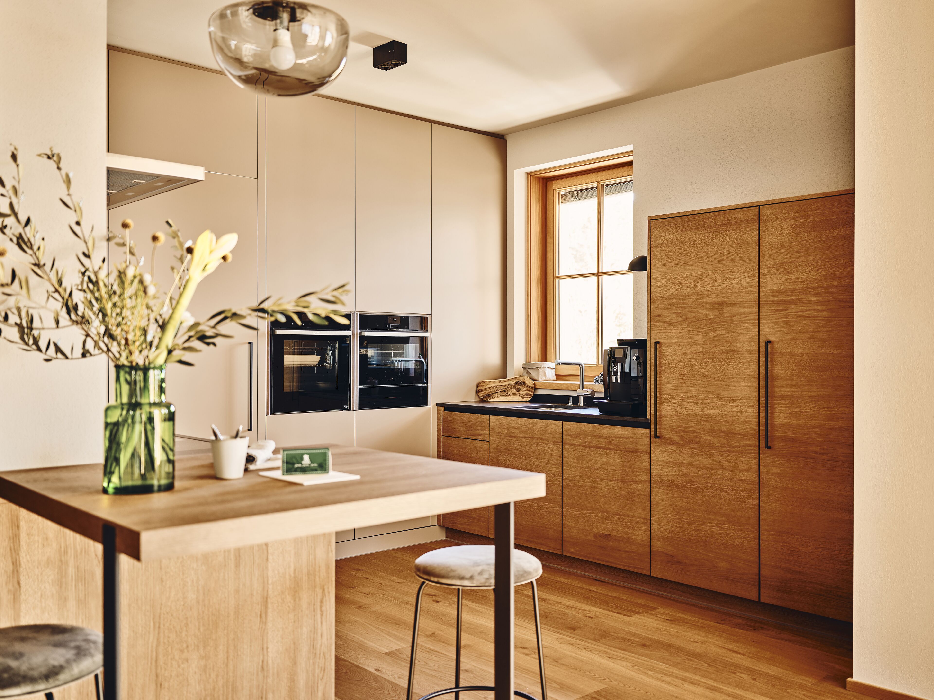 Una cocina moderna con armarios de madera, horno empotrado, cafetera y ventana que proporciona luz natural.